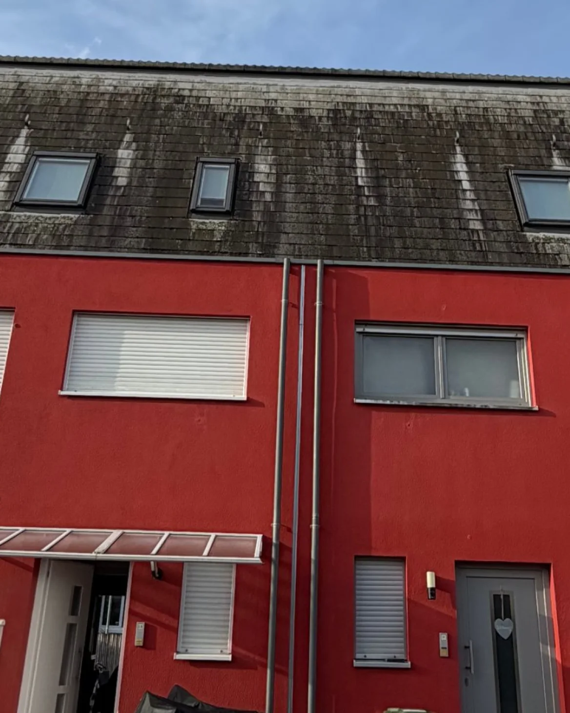 Dach mit schwarzen Ablaufstreifen über roter Fassade